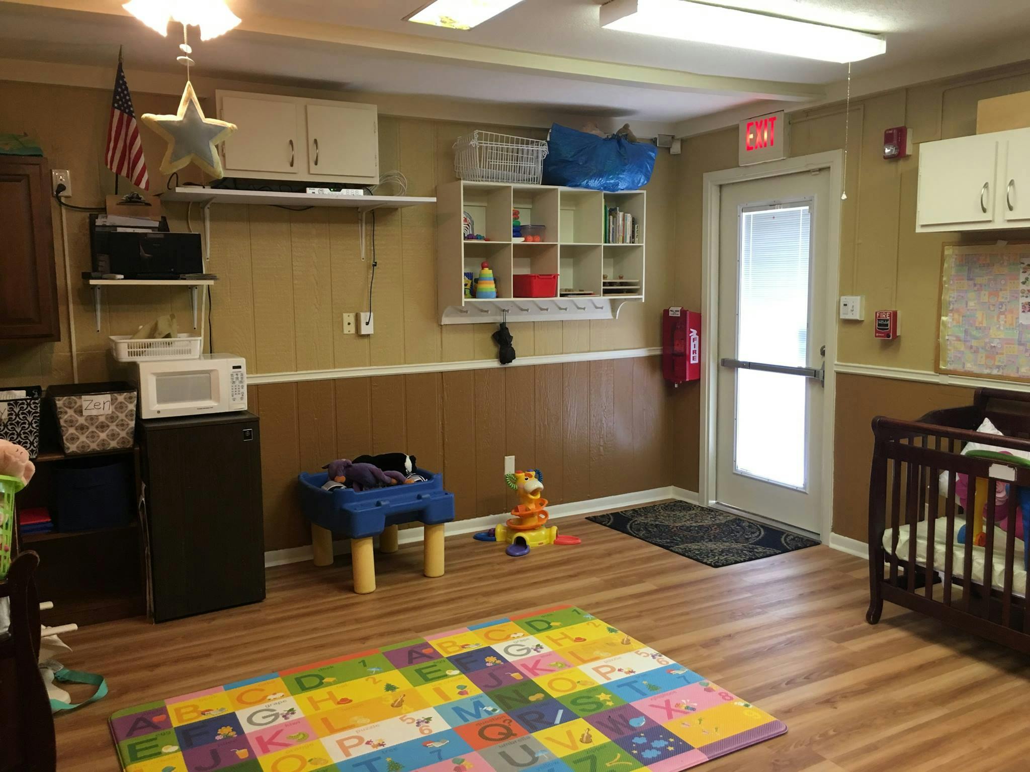 Childcare room with crib, colorful playmat, and small furniture