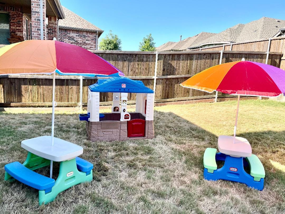 Playhouse and two picnic tables with umbrellas in a backyard