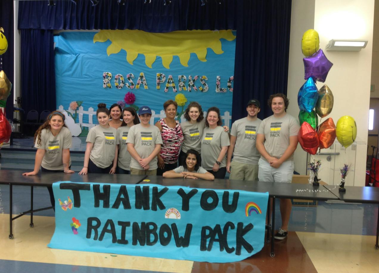 Group of people standing behind a table with a banner that says "THANK YOU RAINBOW PACK"