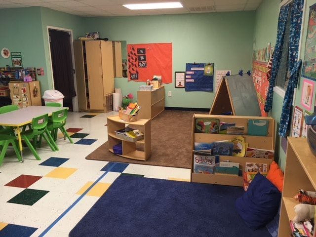 Classroom with small tables and chairs, bookshelves, and a blue rug