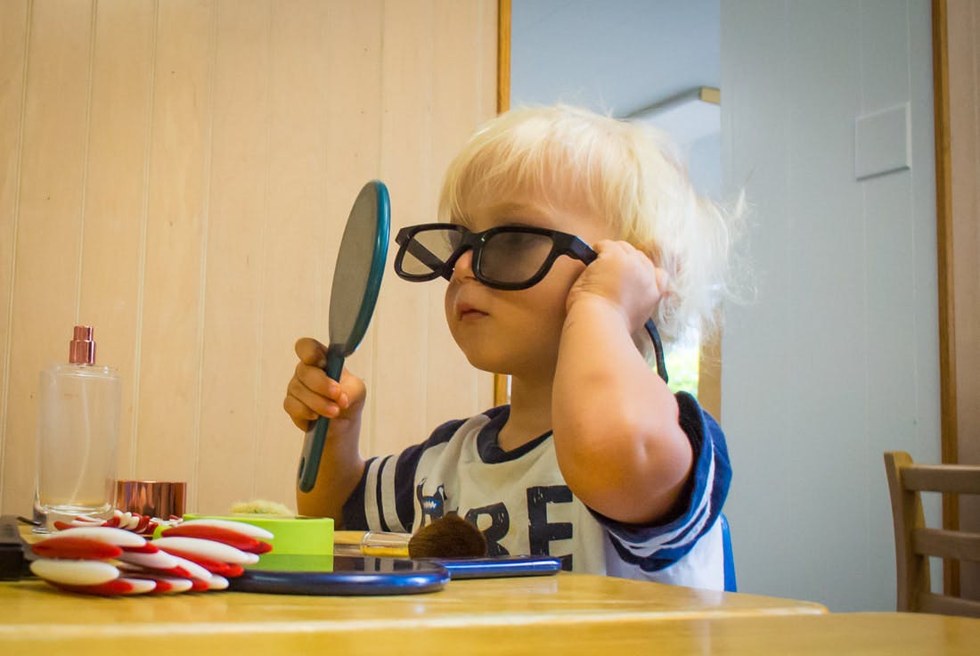 Child wearing oversized glasses and holding a mirror