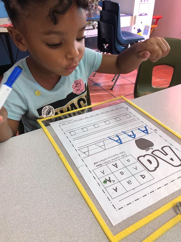 Child holding a marker and tracing letters on a worksheet