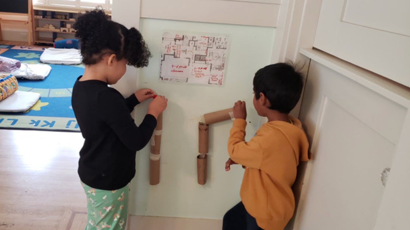Two children playing with cardboard tubes on a wall