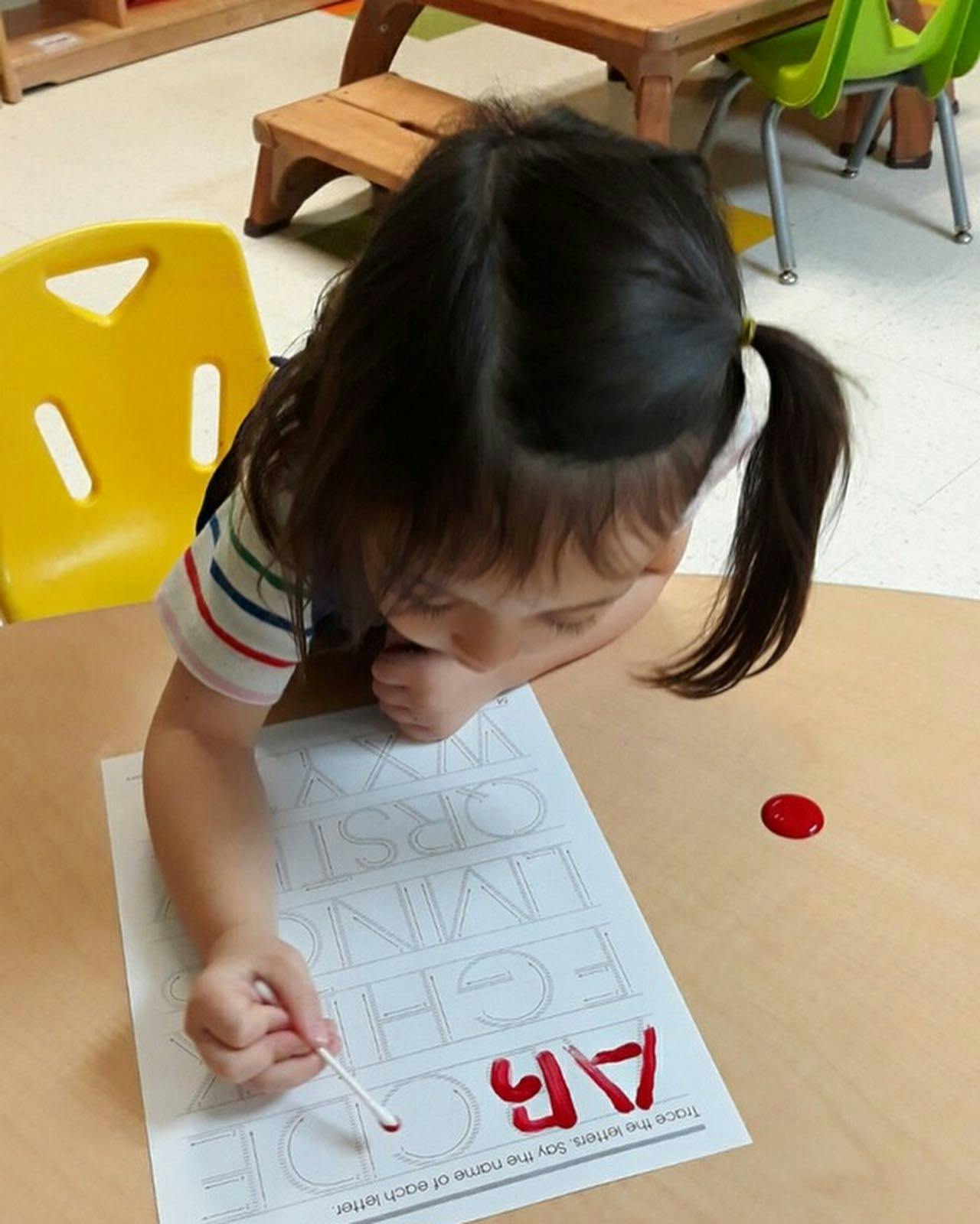 Child tracing letters on paper with a cotton swab