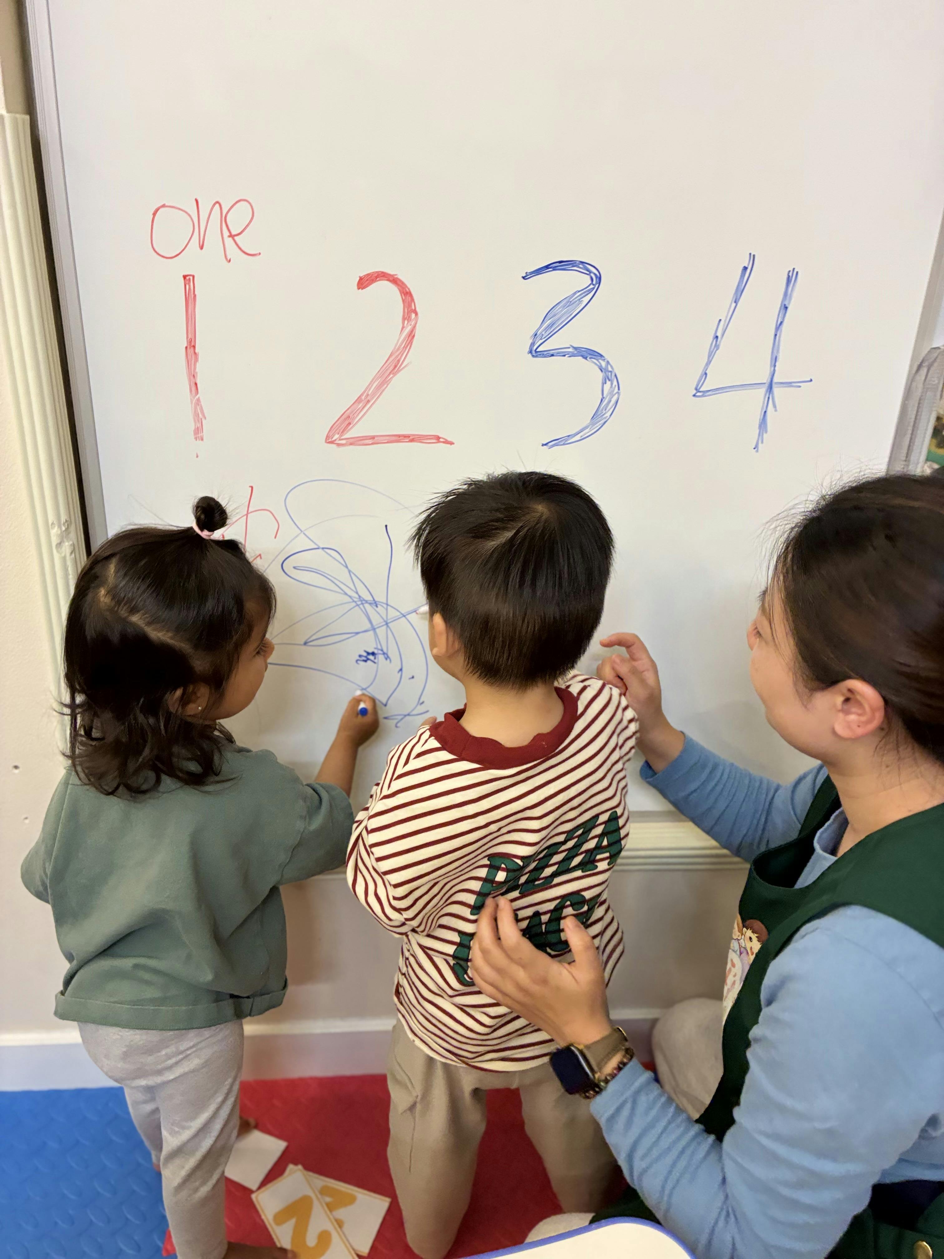 Adult and two children writing numbers on a whiteboard