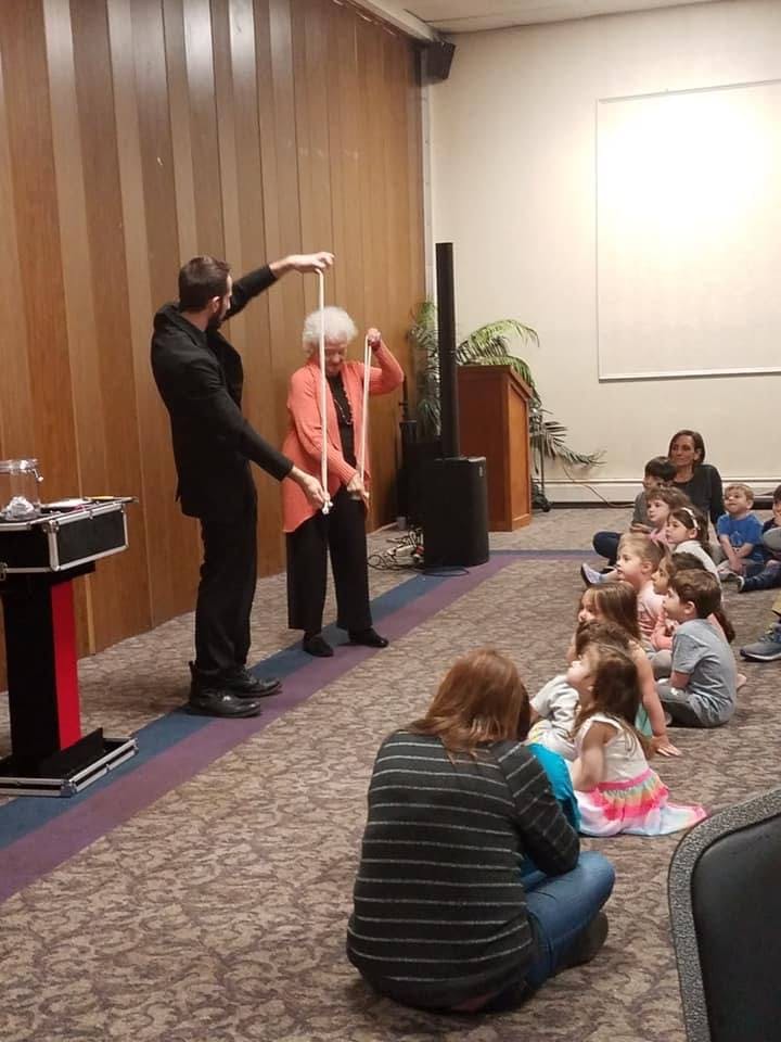Magician and person holding ropes for an audience of children