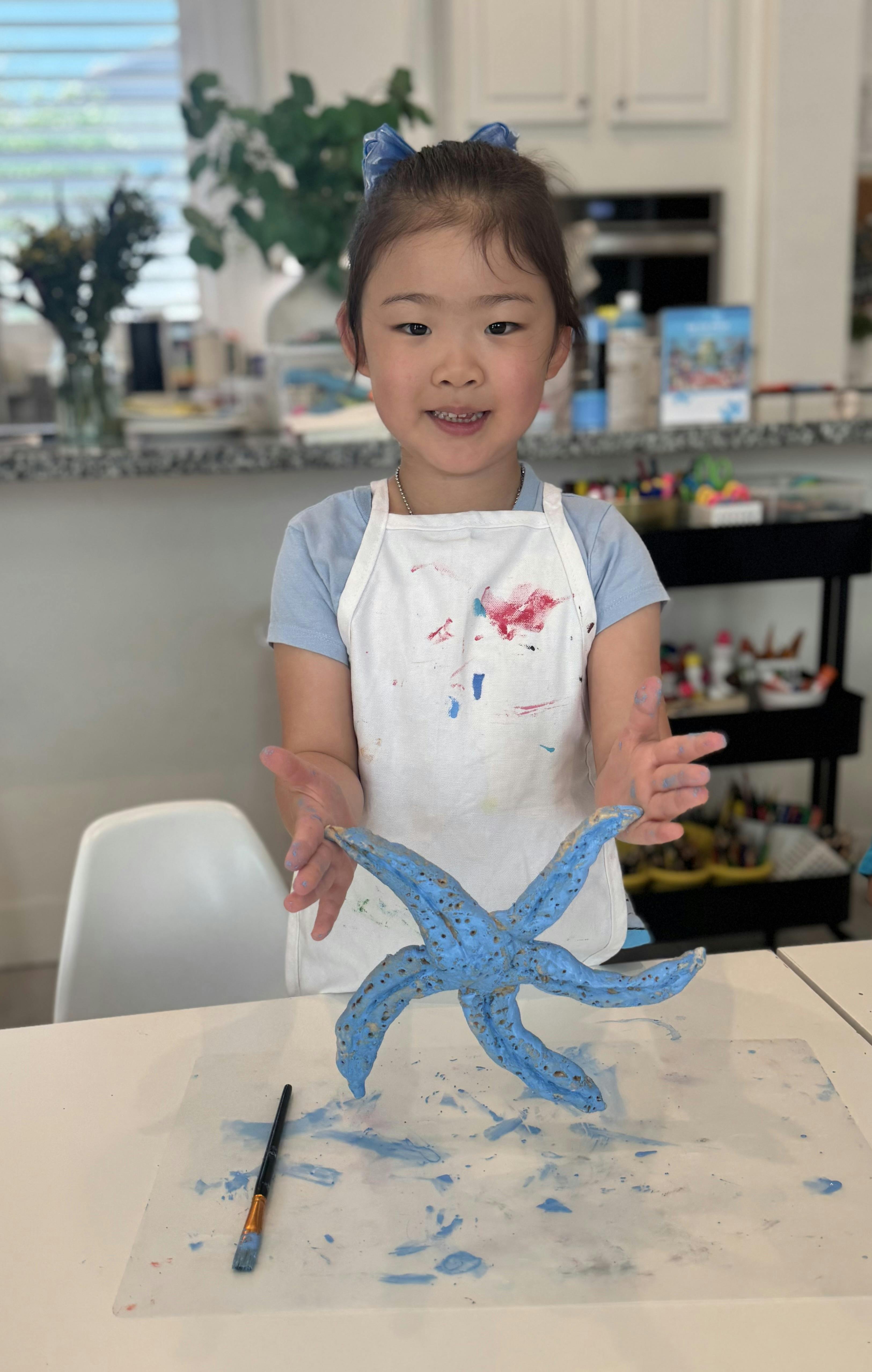 Child wearing an apron displaying a blue painted starfish craft