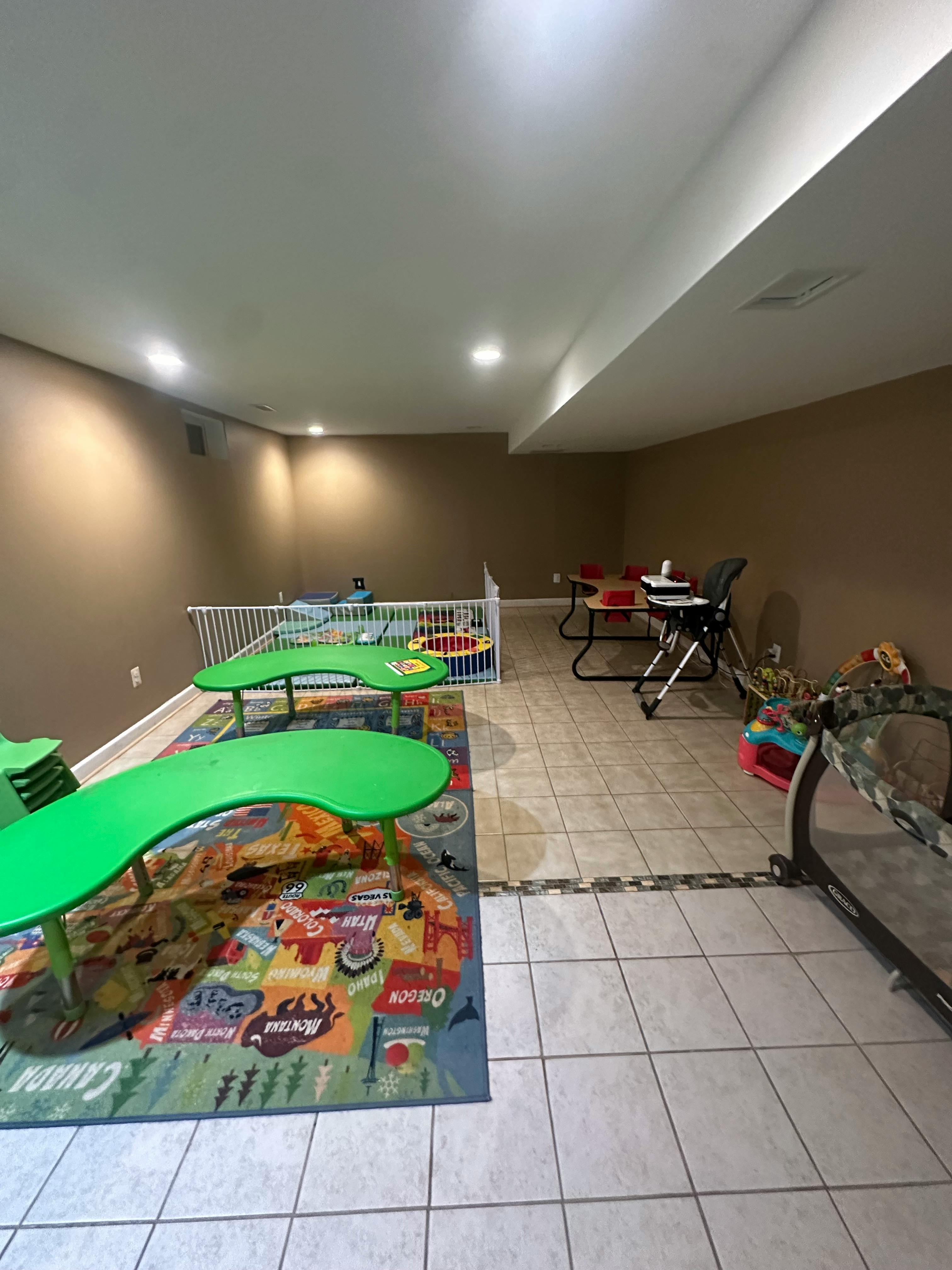 Playroom with green tables, colorful rug, and baby gate