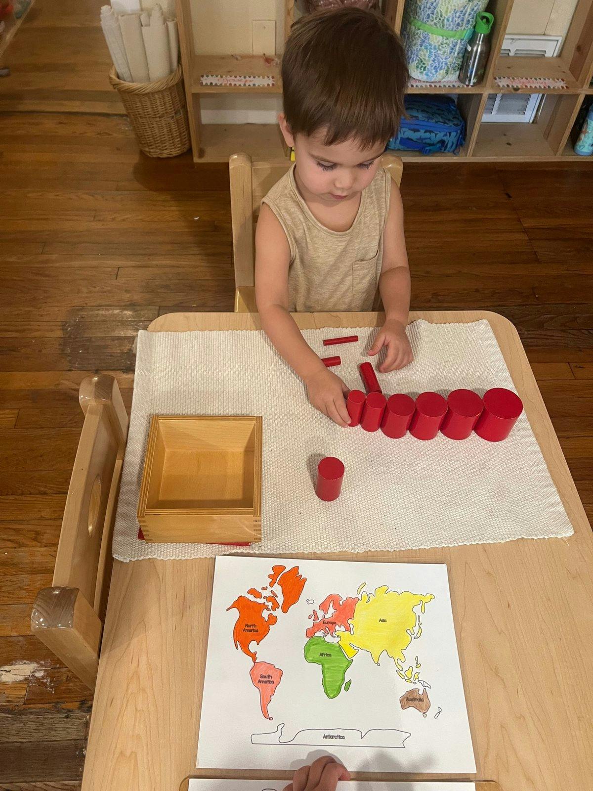 Child sitting at a table with red wooden cylinders and a world map