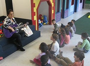 Person playing guitar for a group of children sitting on the floor