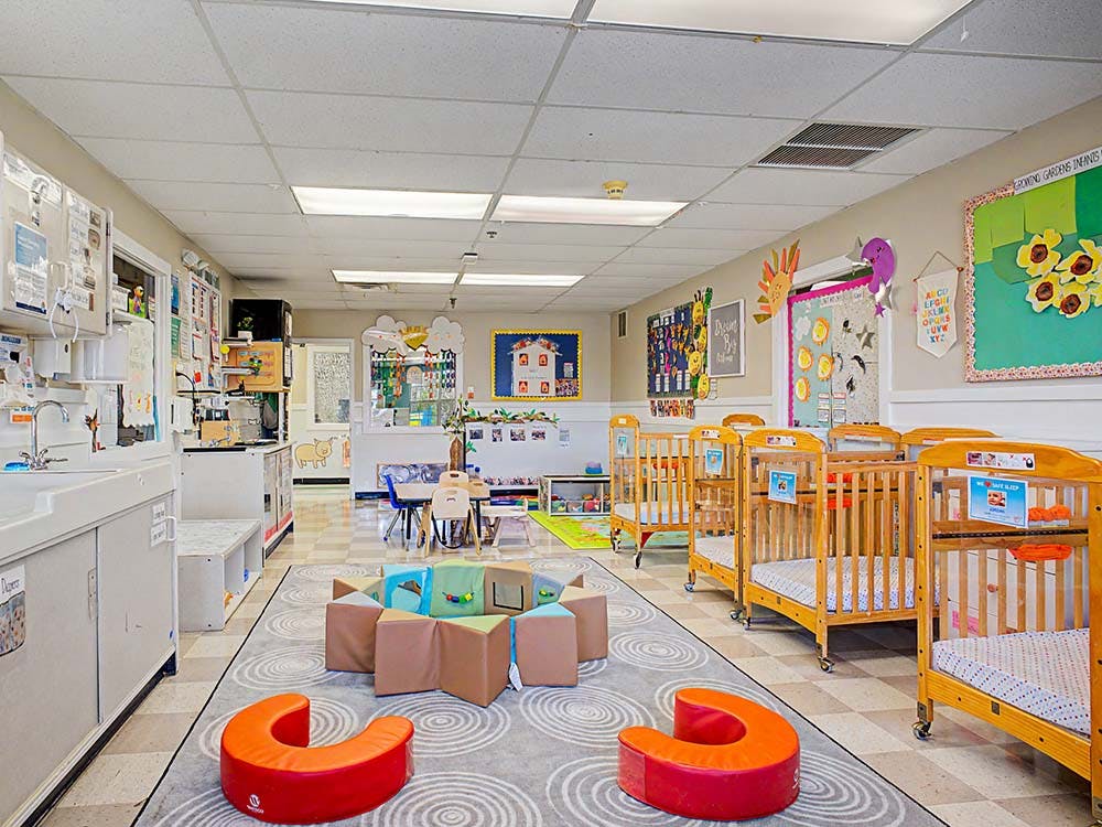 A daycare room with cribs, play mats, and a changing station