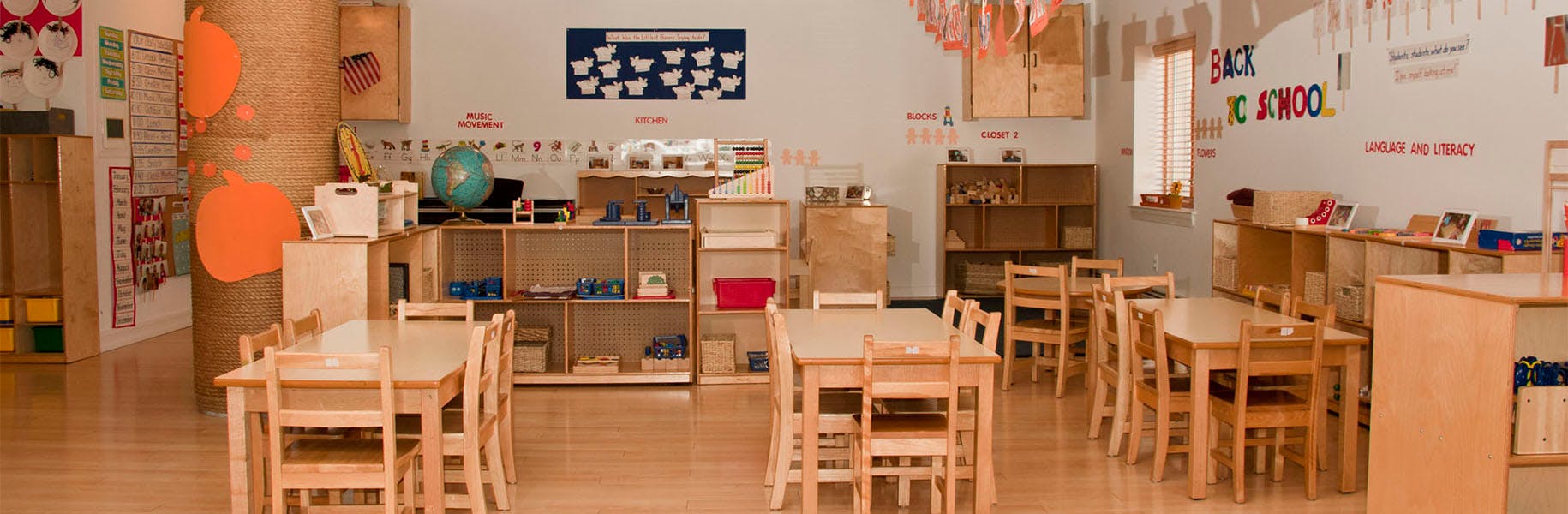 Empty classroom with small tables and chairs, shelves with toys and learning materials