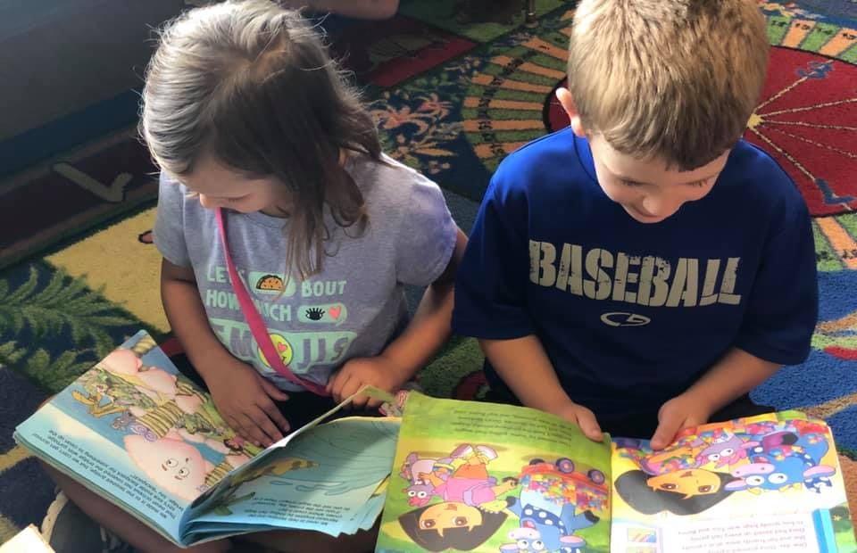 Two children sitting on a rug reading books