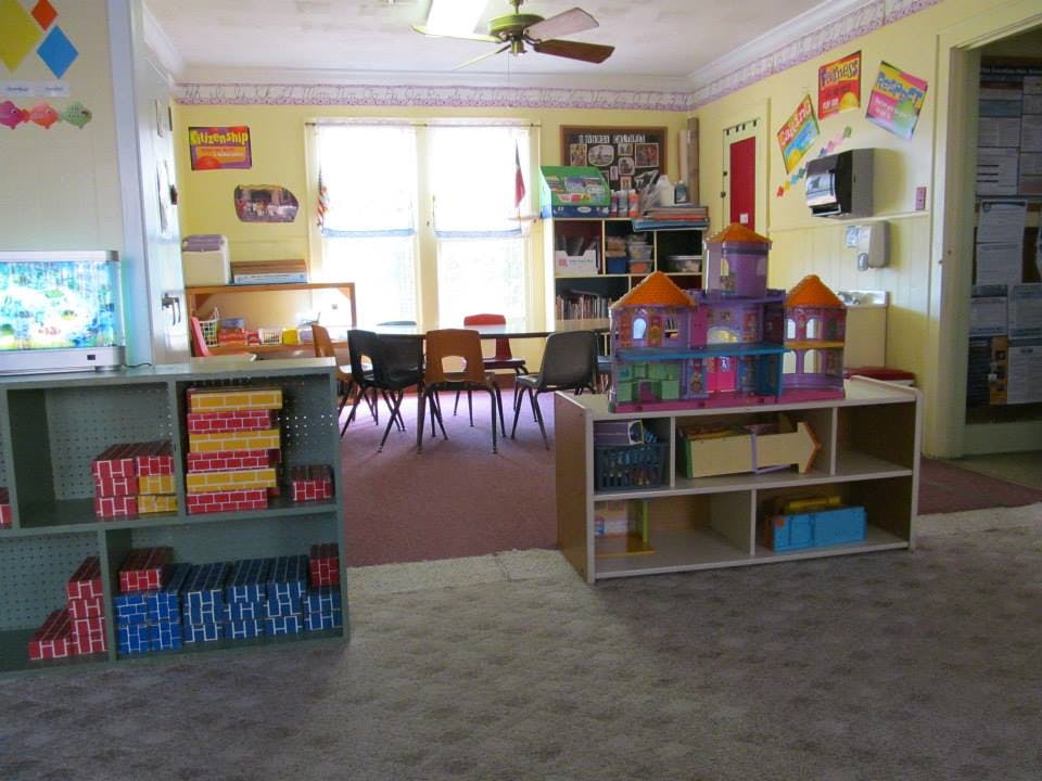 Classroom with shelves of books and toys, tables and chairs, and a large window