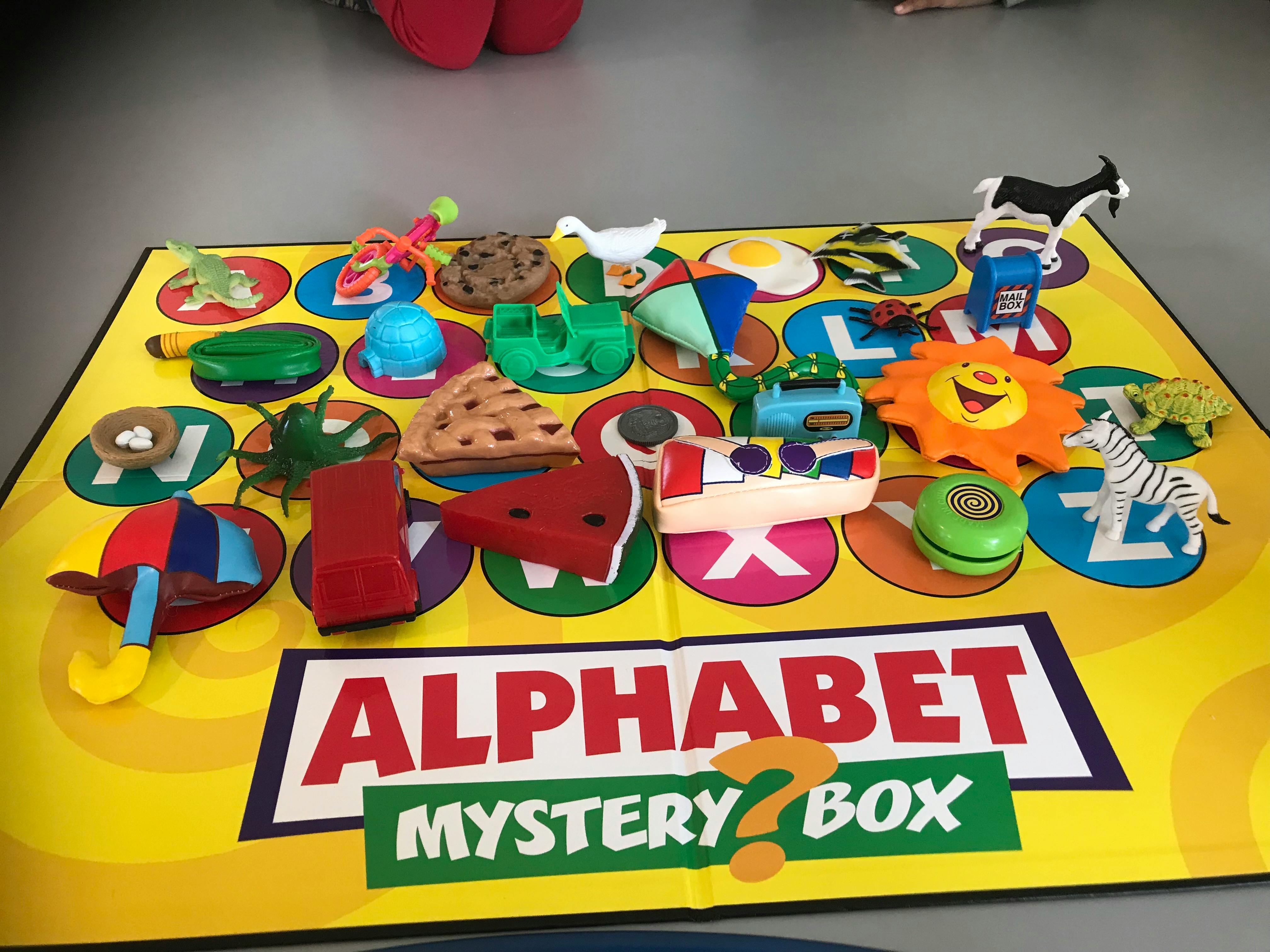 Alphabet Mystery Box game with various small toys on a mat