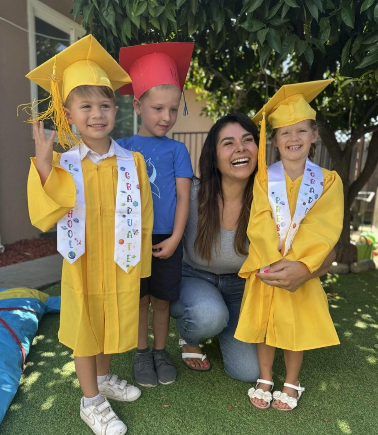 Person kneeling with three children wearing graduation caps and gowns