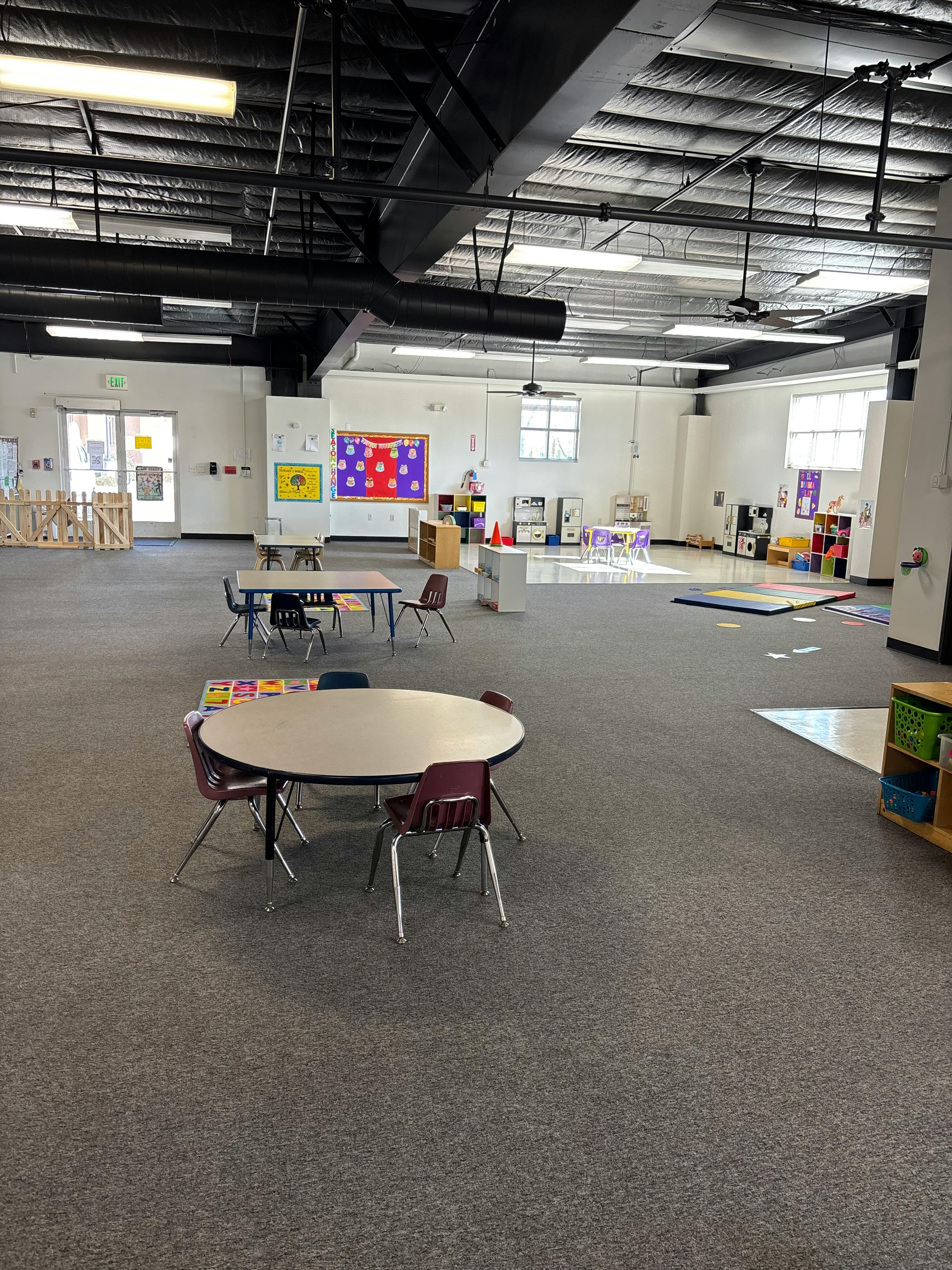 An empty classroom with tables, chairs, and learning decorations on the wall