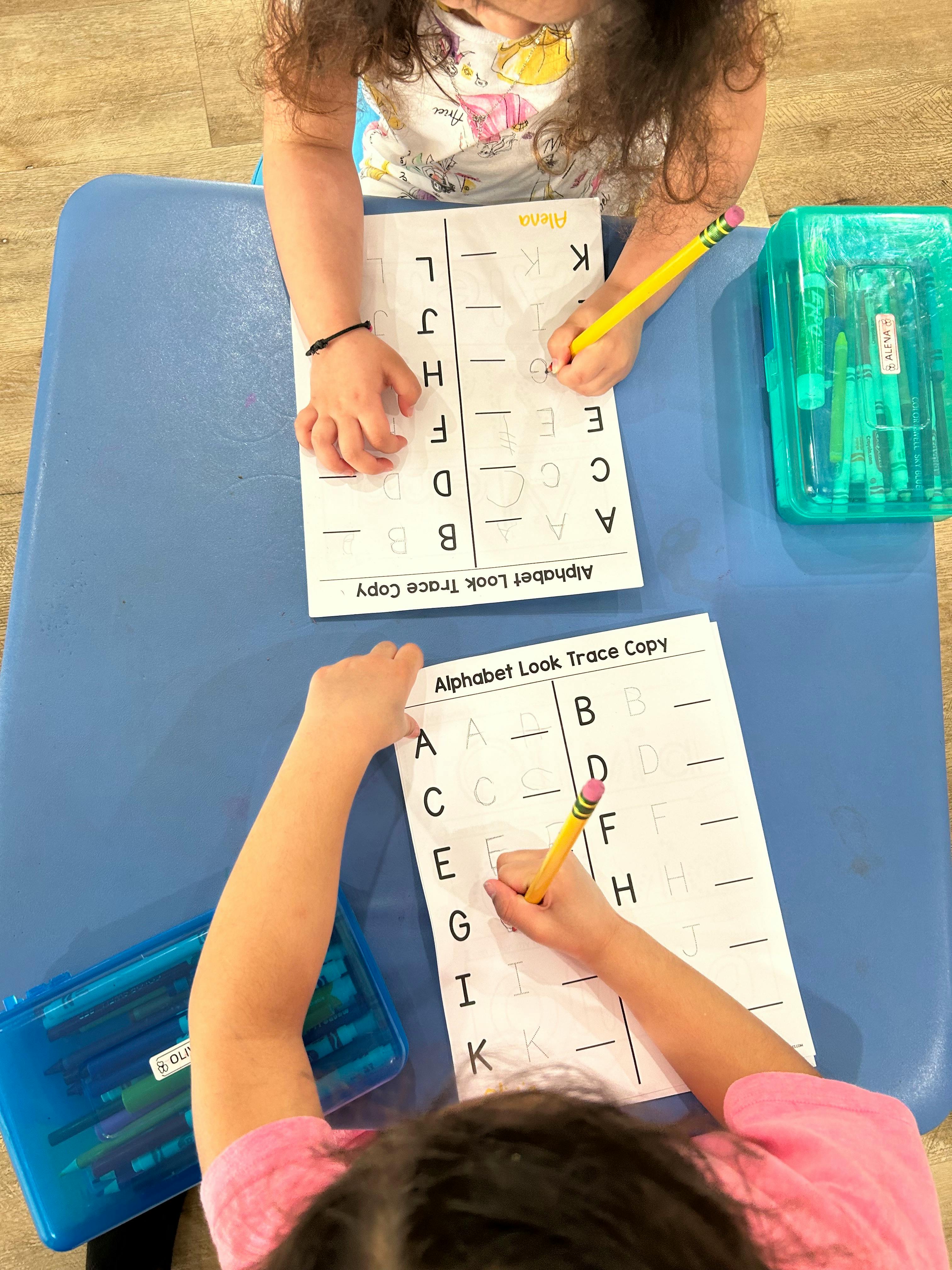 Two children tracing letters on alphabet worksheets