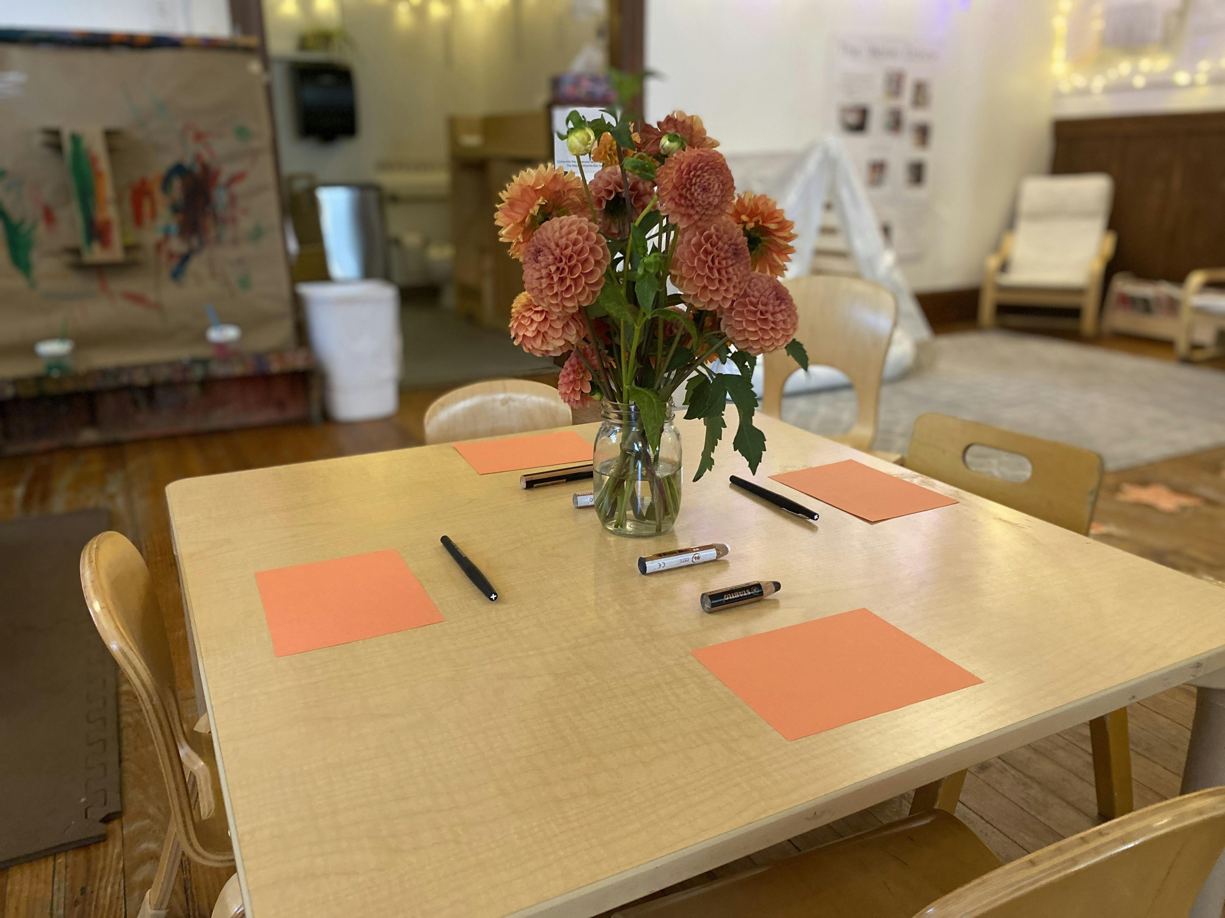 Table with flowers, paper, and markers in a classroom