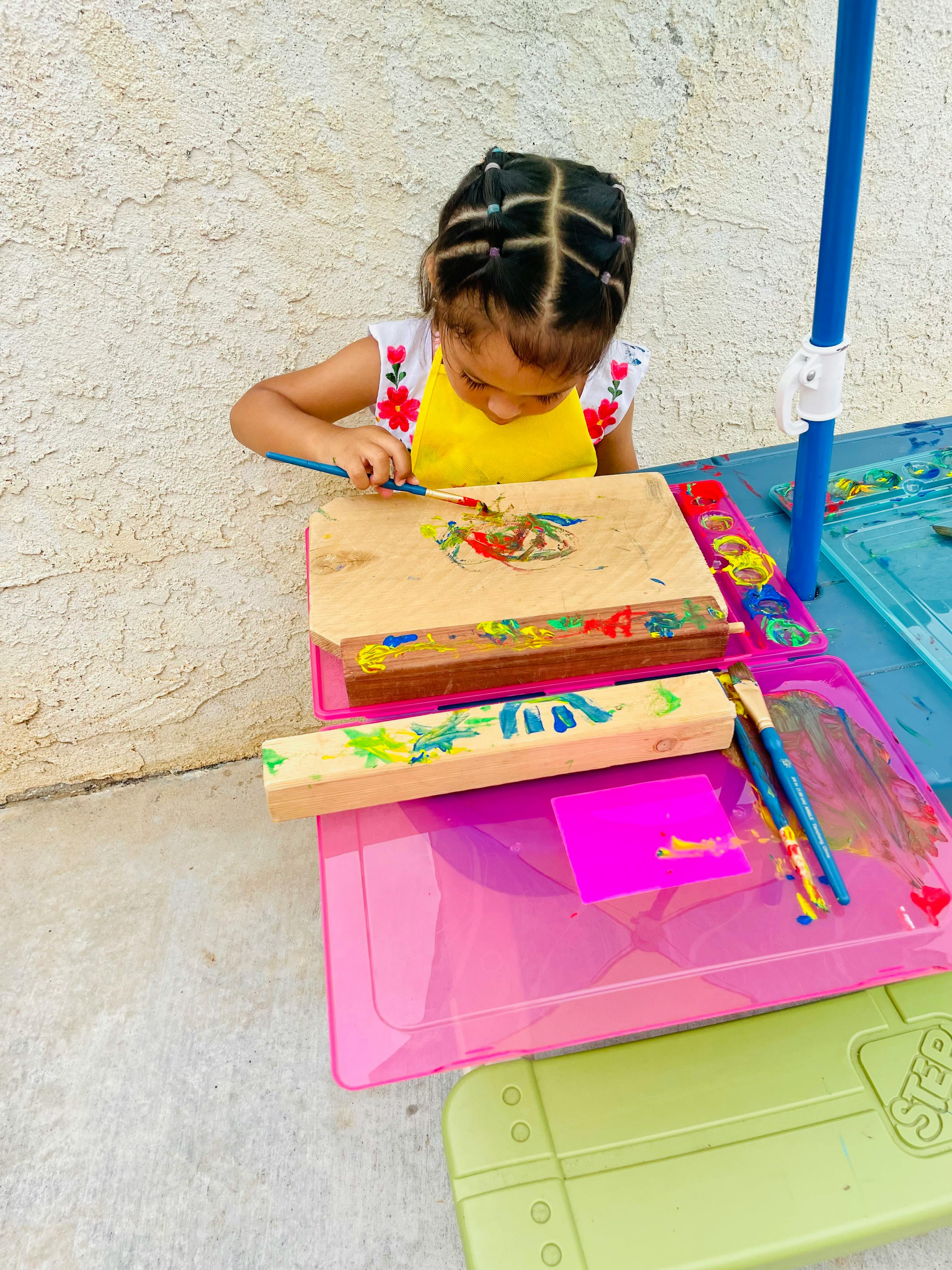 Child in a yellow apron painting on a wooden block