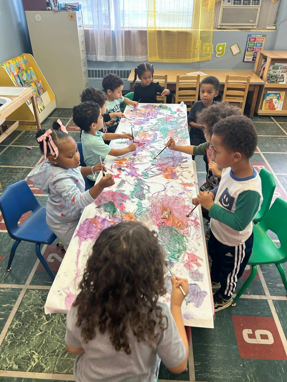 Children painting on a long sheet of paper in a classroom
