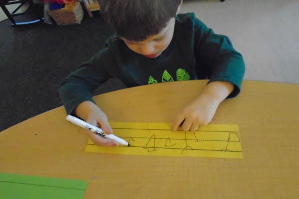 Child drawing on yellow paper with a marker