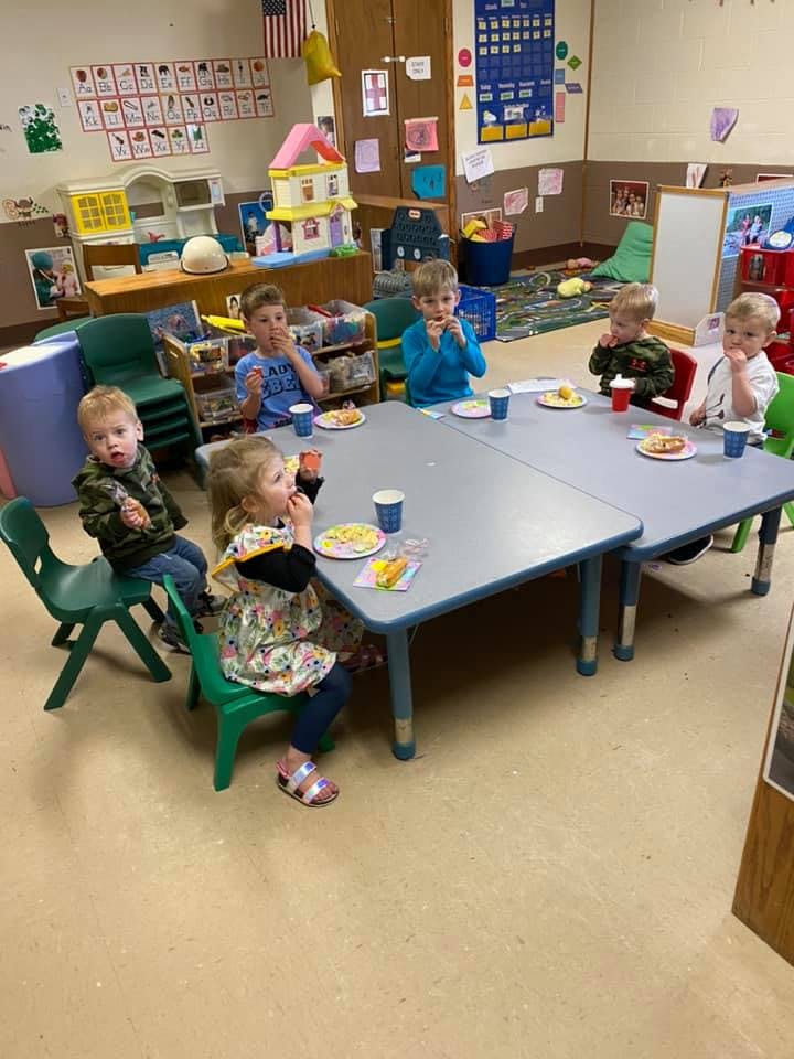 Children sitting at tables eating snacks in a classroom eating snacks