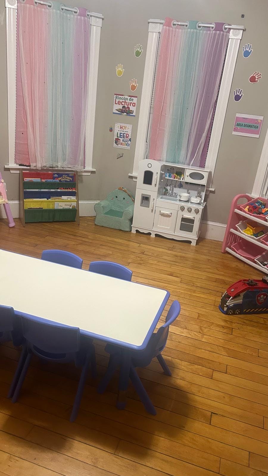 Classroom with a table and chairs, play kitchen, book rack, and hand cutouts