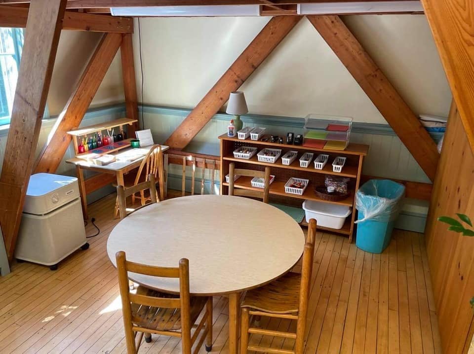 Classroom with a round table and chairs, a desk, and a storage shelf