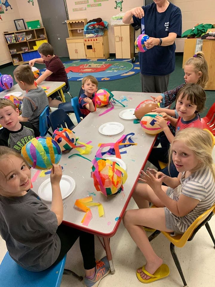 Children and an adult making crafts at a table in a classroom