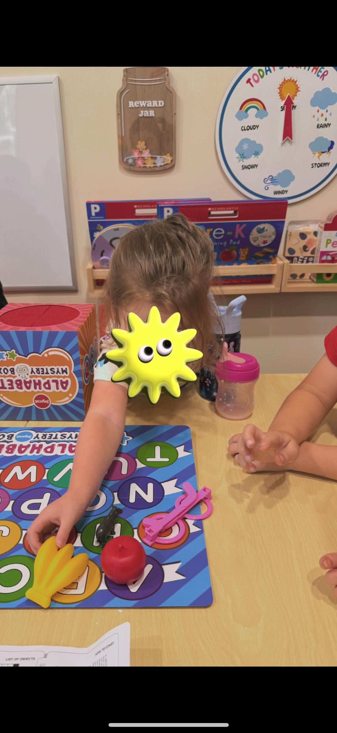 Child playing with alphabet letters and plastic fruit at a table