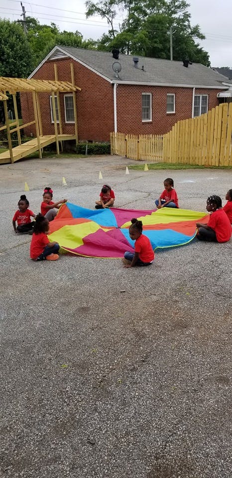 Children sitting around a colorful parachute on asphalt