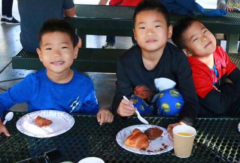 Three children sitting at a table with plates of food