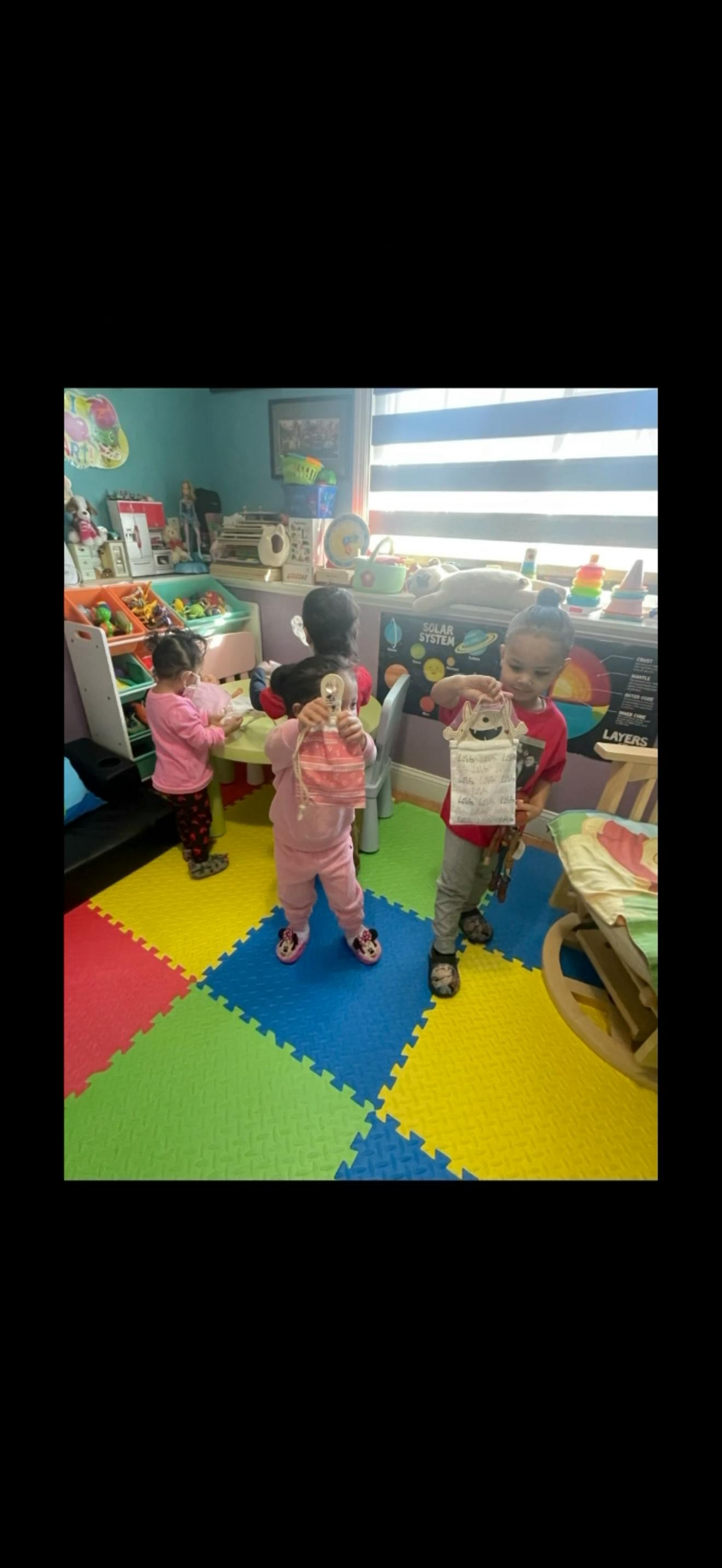 Children holding craft projects in a brightly colored playroom