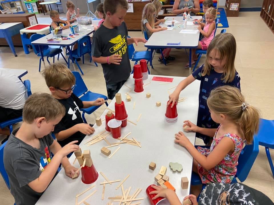 Children building with red cups and wooden sticks at tables