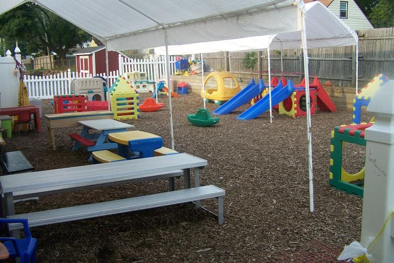 Outdoor play area with slides, play structures, and picnic tables under a tent