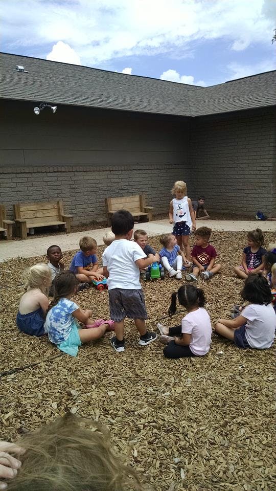 Children sitting in a circle on wood chips outdoors