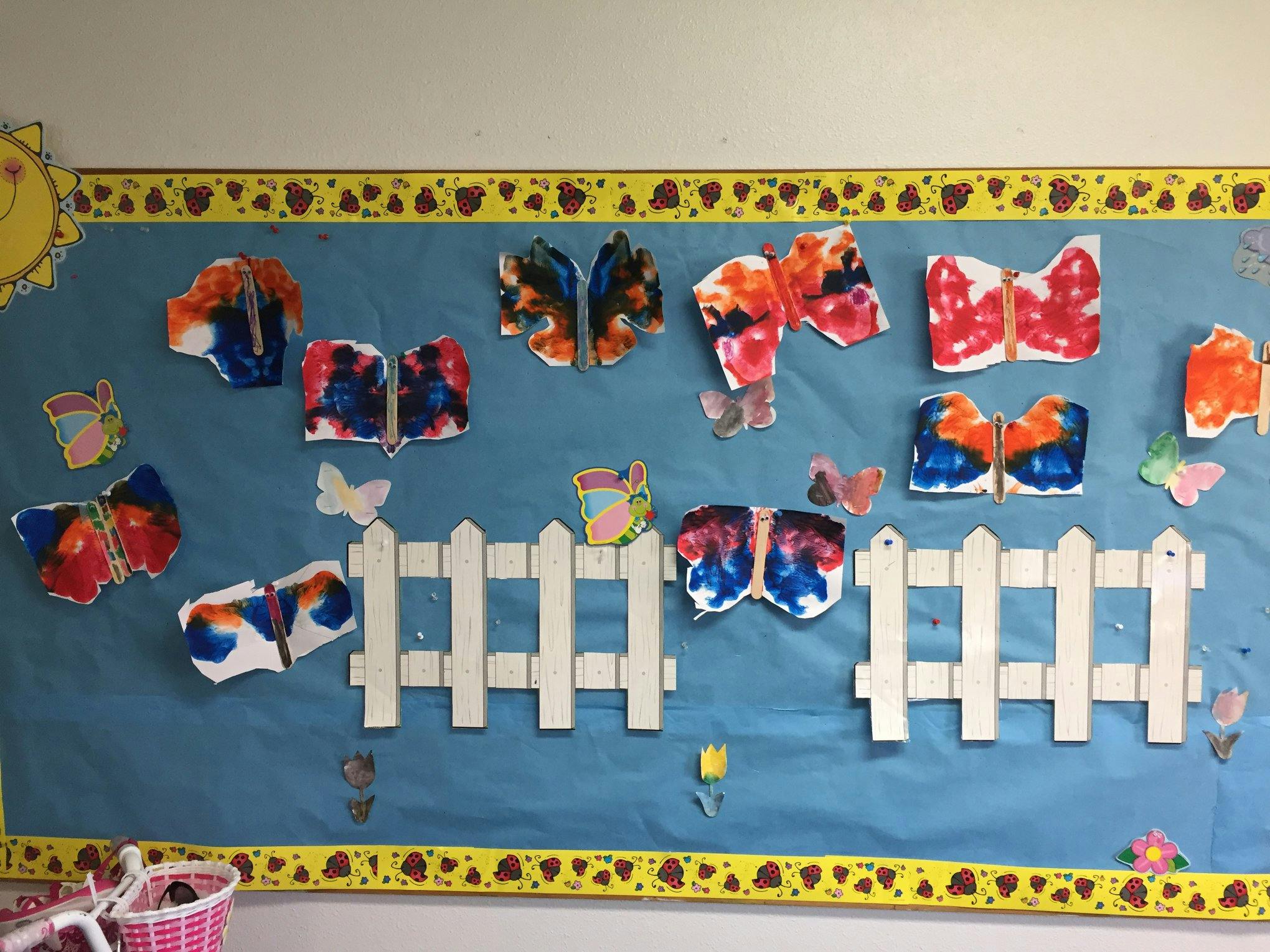 Children's butterfly artwork and a white picket fence on a blue bulletin board