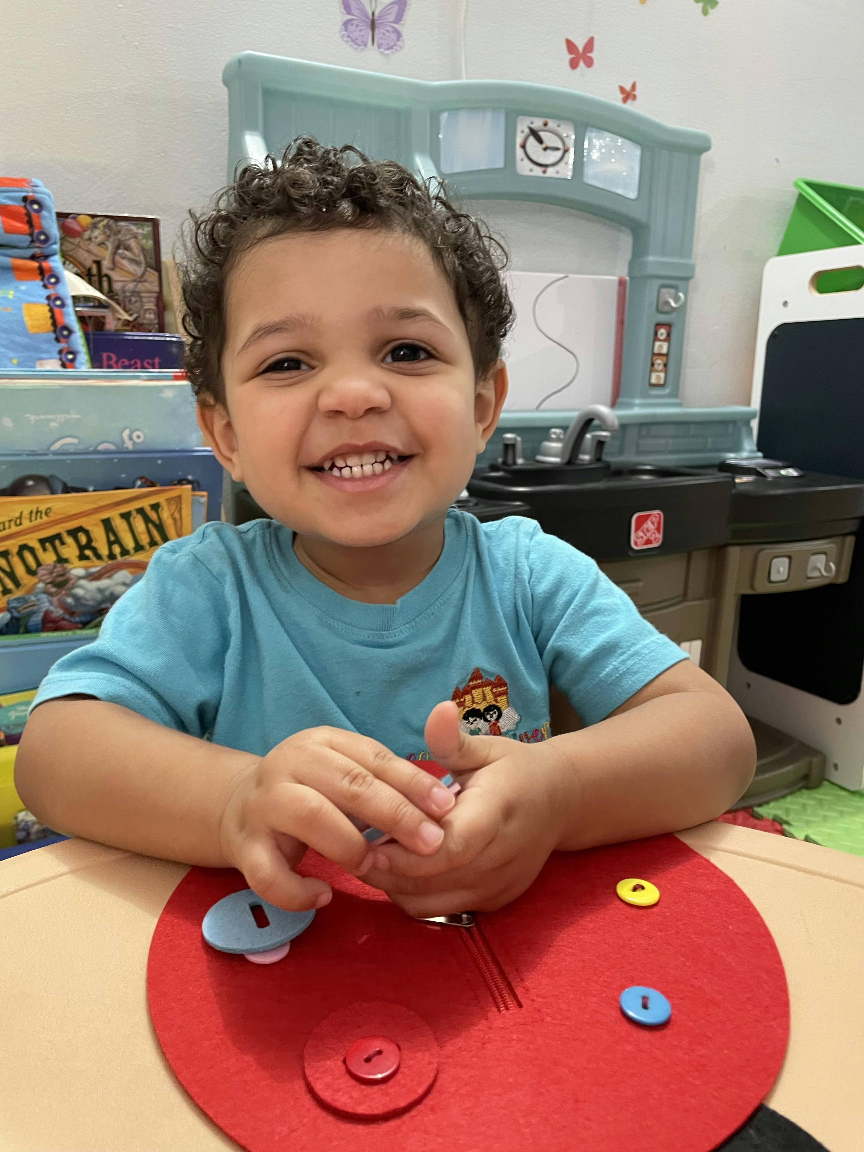 Child smiling while playing with a red button toy