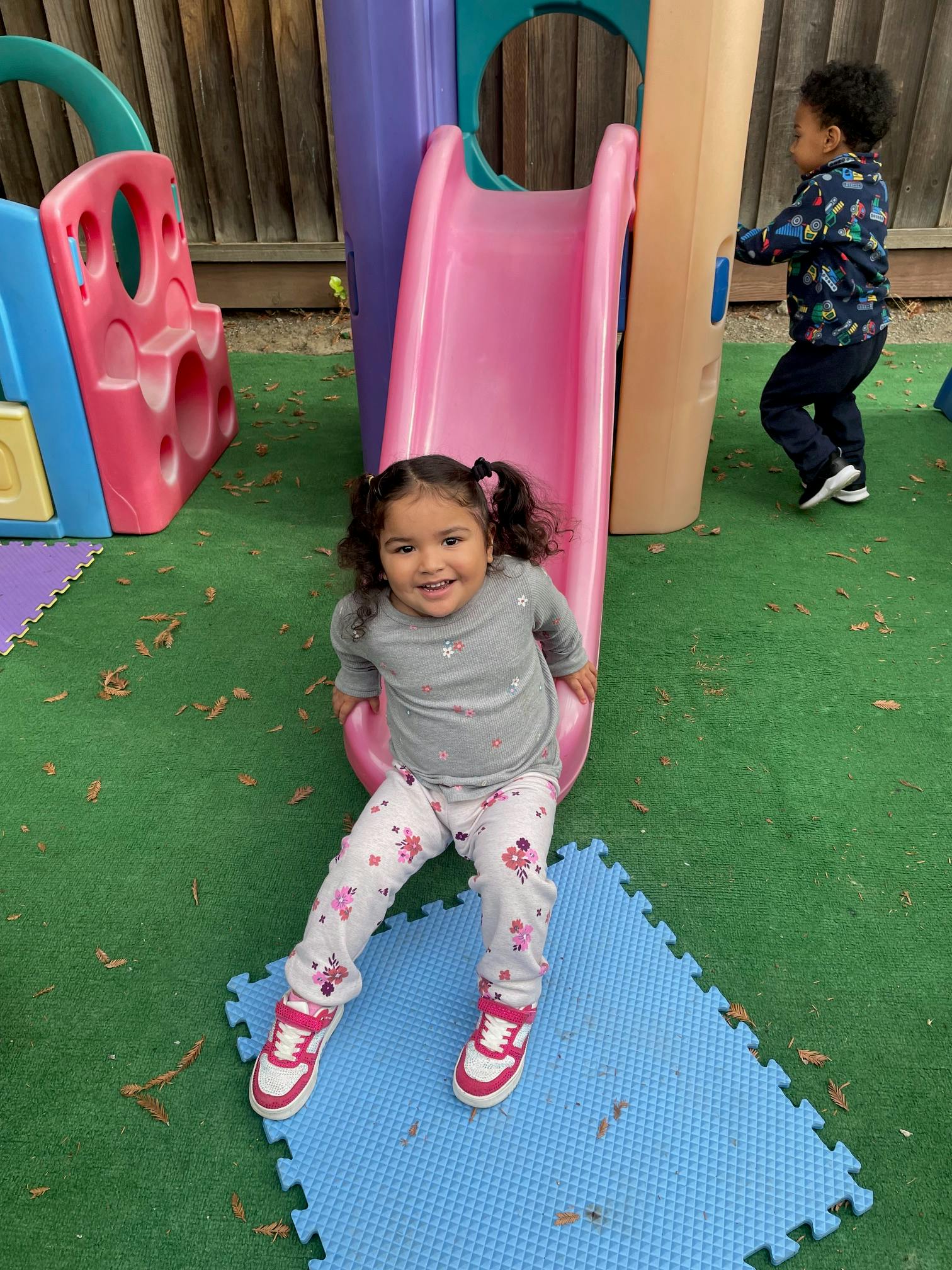 Child sitting at the bottom of a pink slide on a playground