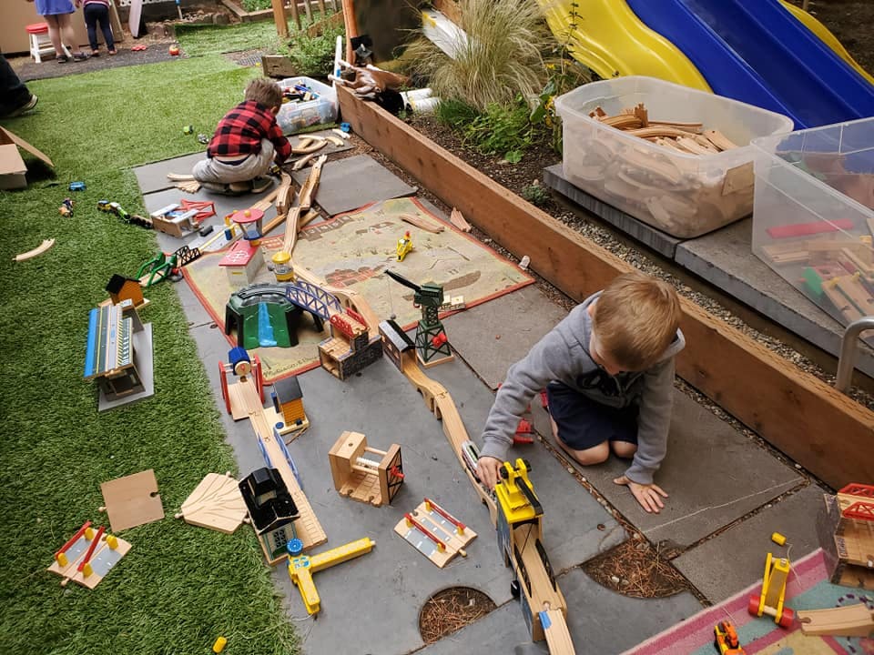 Two children playing with a wooden train set outdoors