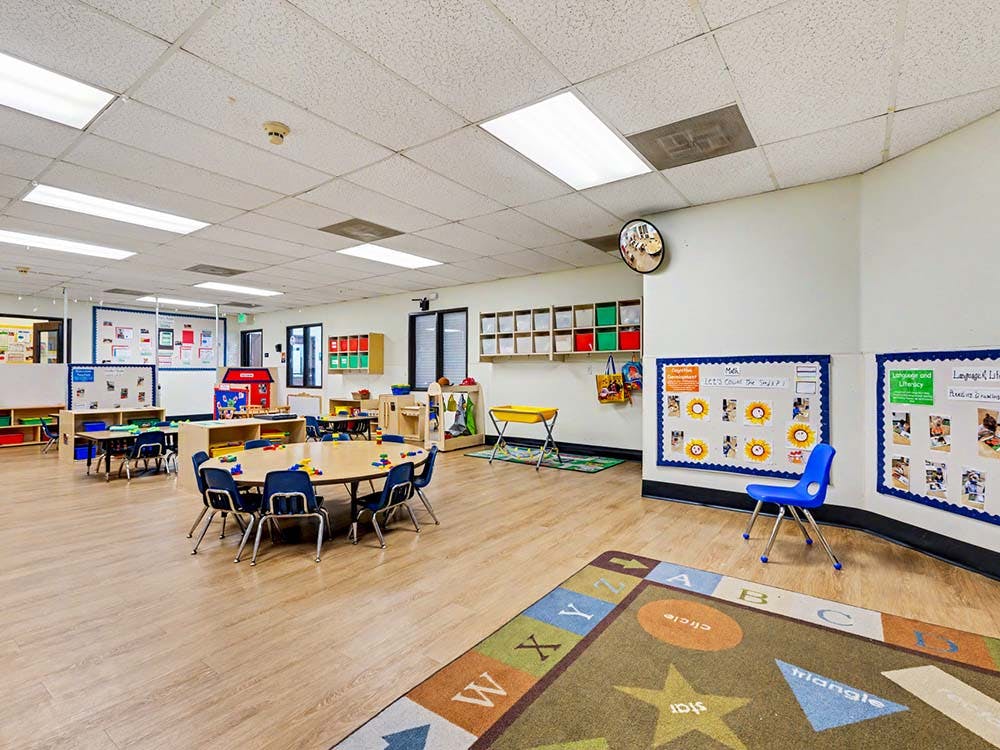 Classroom with tables, chairs, and learning materials, alphabet rug