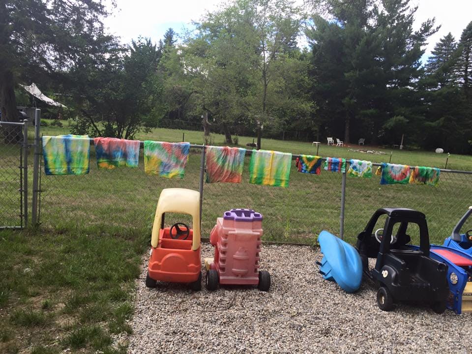 Tie-dye towels hanging on a fence with toy cars on the ground