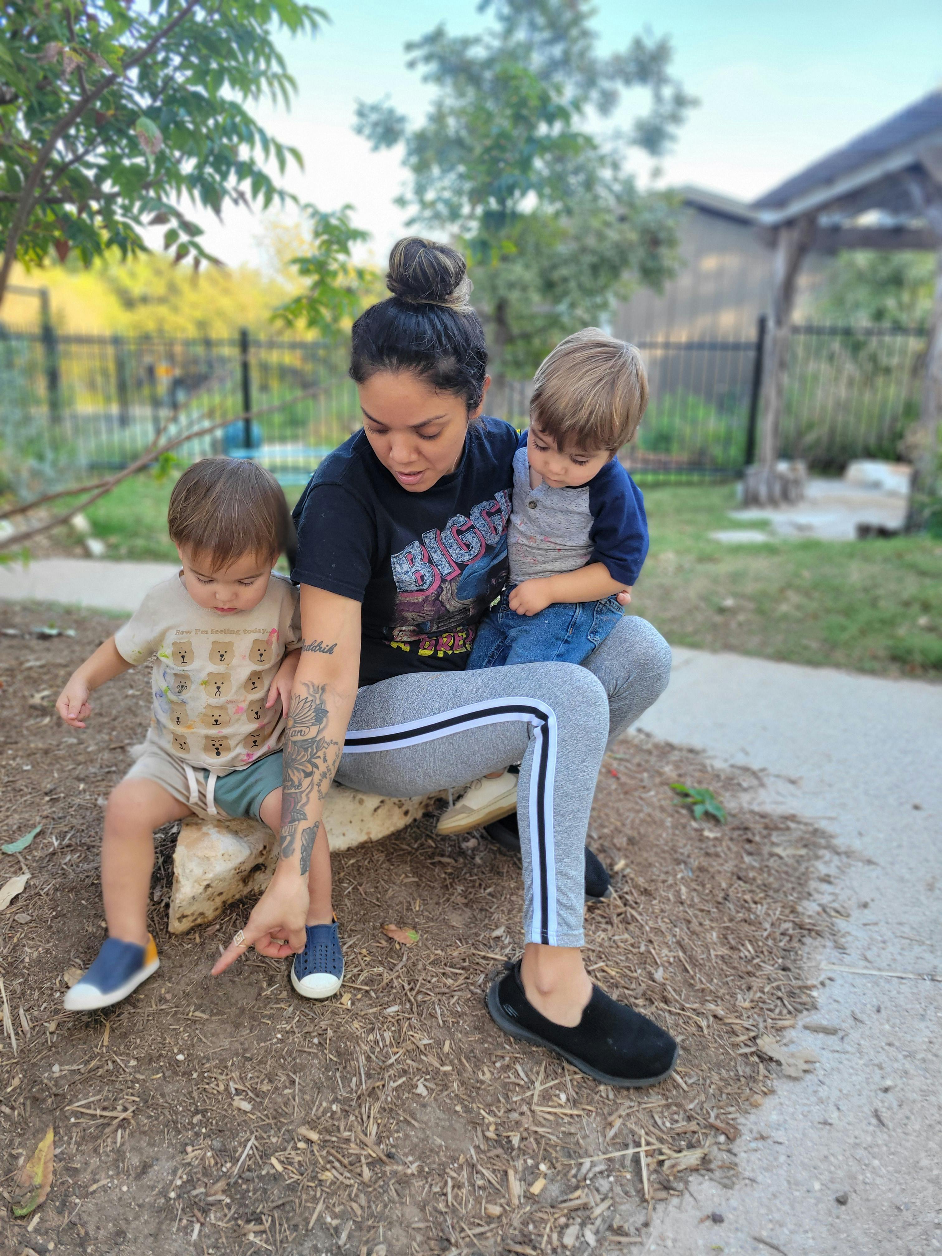 Person sitting with two children, pointing at the ground