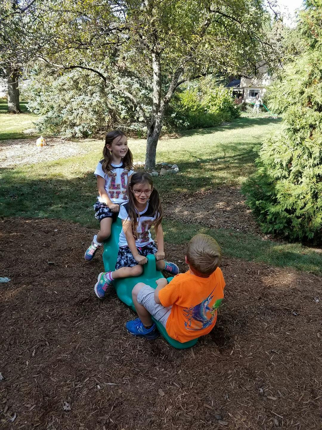Three children playing on a green seesaw in a park