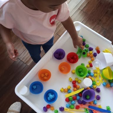 Child playing with colorful sorting toys in a white tray