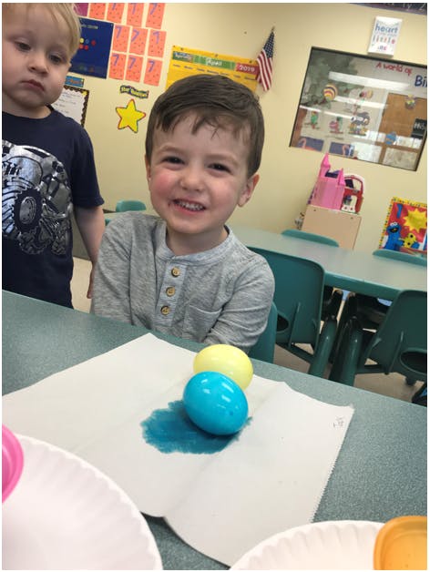 Child smiling at a table with dyed eggs on a paper towel