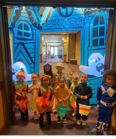 Group of children wearing various costumes standing before an inflatable archway