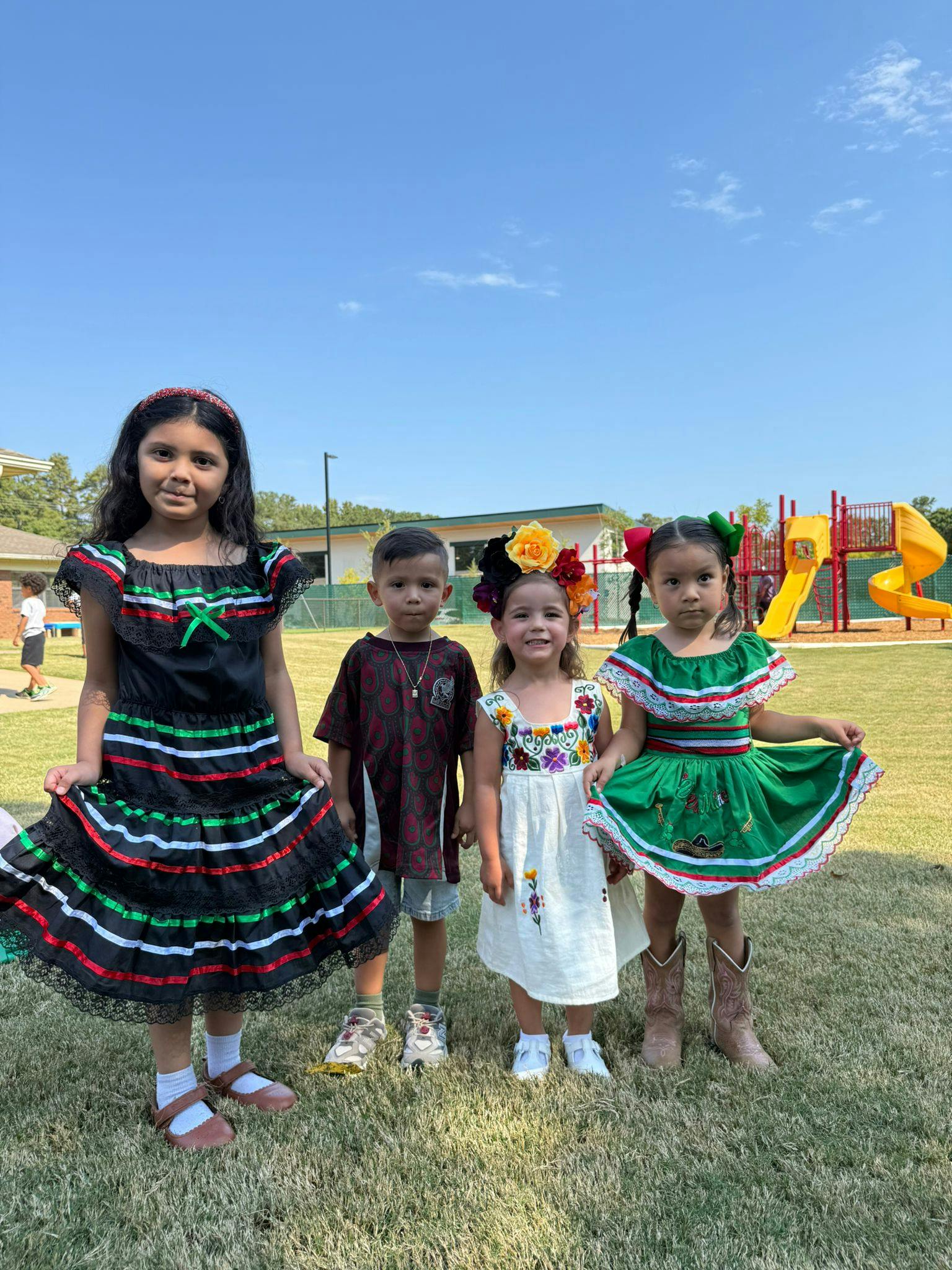 Four children in traditional clothing standing on grass