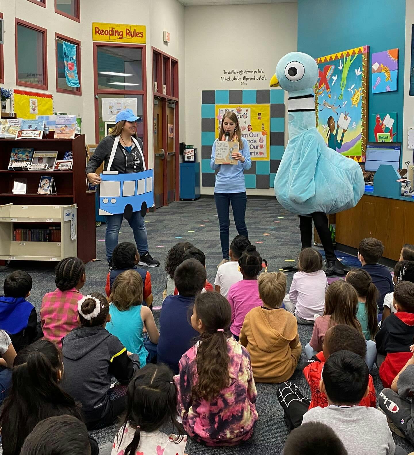 Children sitting on the floor watching a person in a pigeon costume and two other people